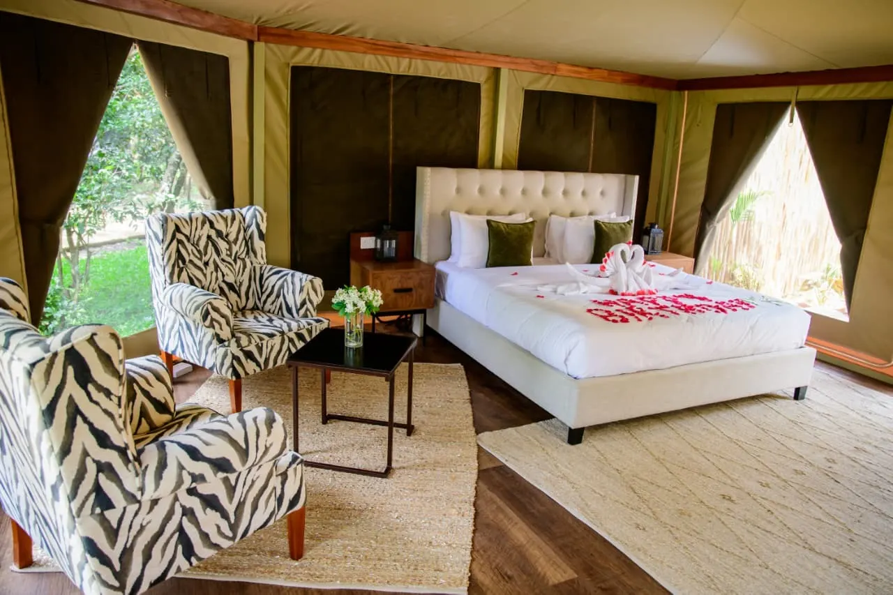 A Lenana tented suite interior with a hand-dressed king bed, safari armchairs and canvas windows onto the garden