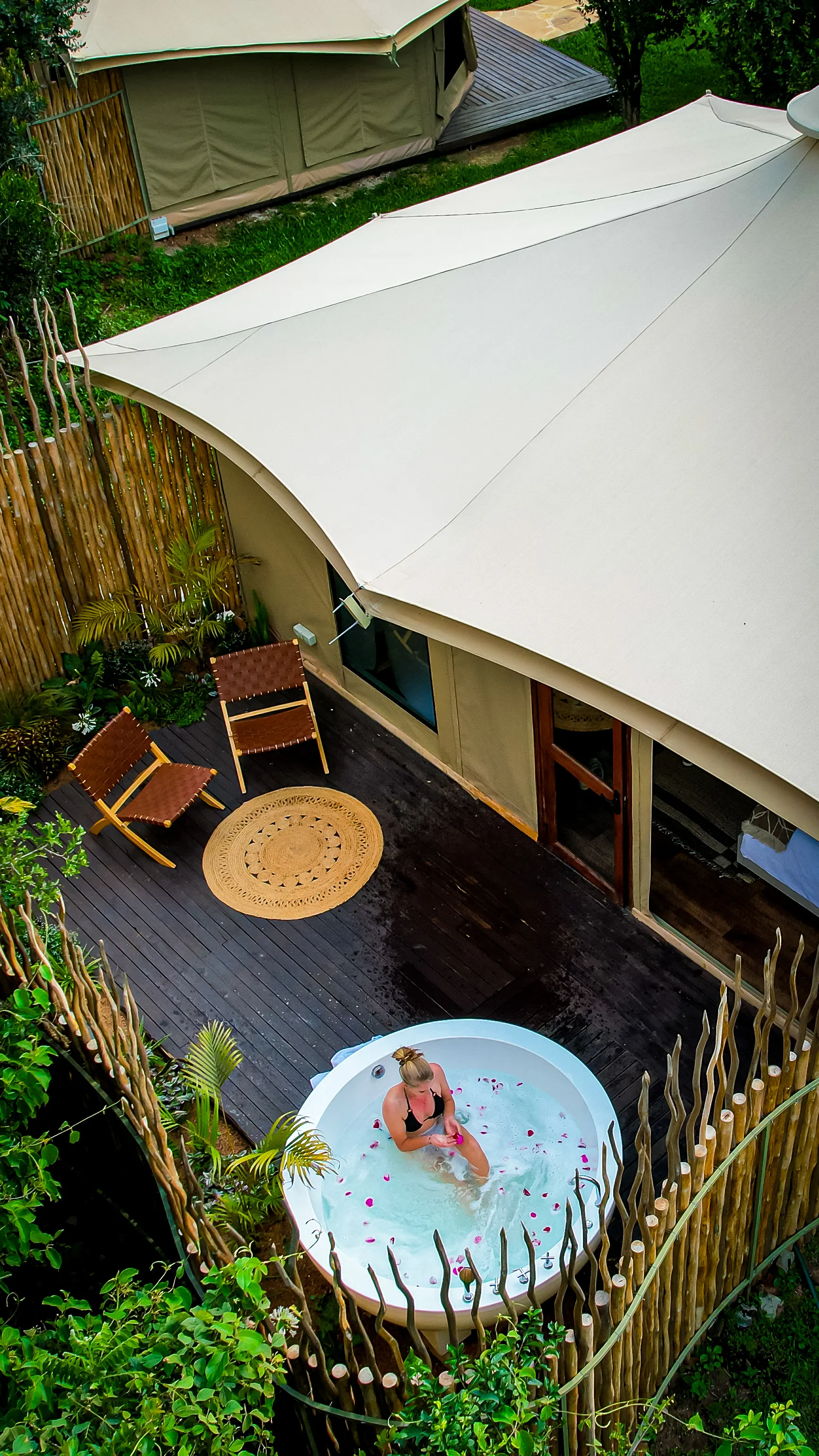 Aerial view of a Nelion tented suite deck with a private outdoor soaking tub set among the trees