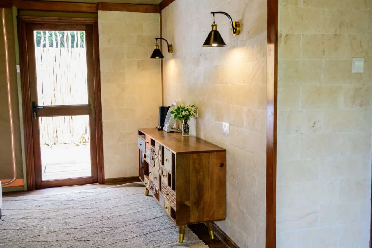 The entrance of a Lenana tented suite with a timber dresser, brass wall lamps and stone walls