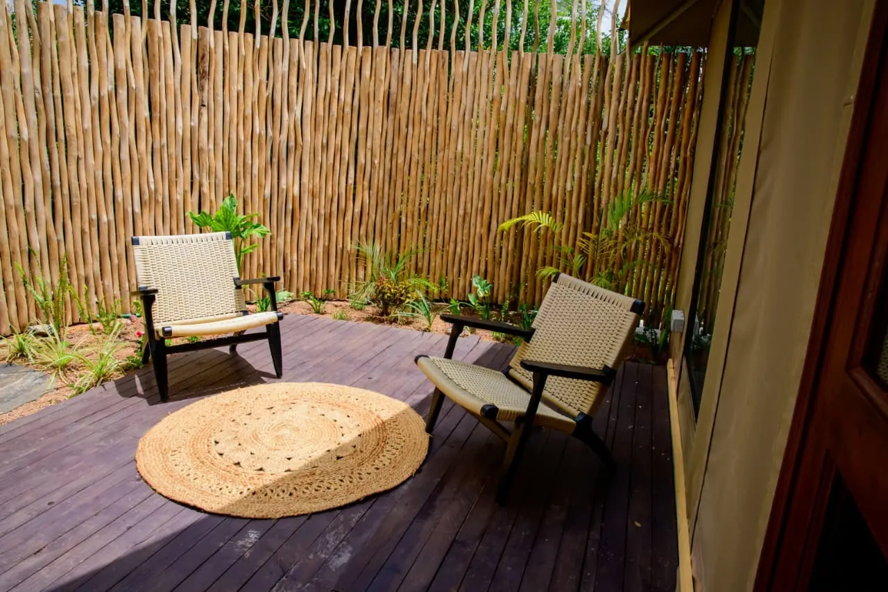 A private timber deck with two woven chairs and a jute rug, screened by a bush garden, at a Nelion tented suite