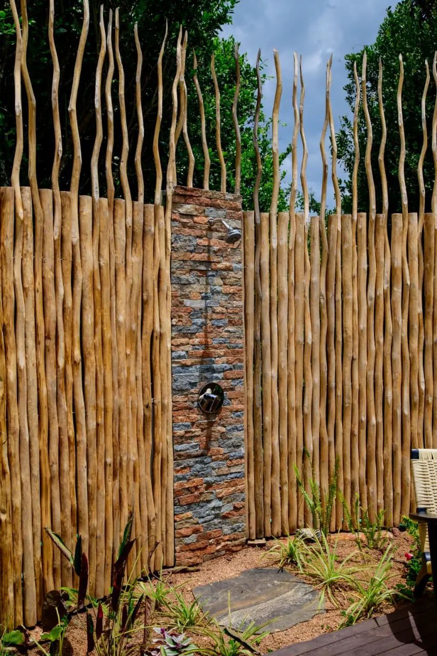 An open-air rainforest shower built from stacked stone behind a timber screen, surrounded by planting, at Nelion