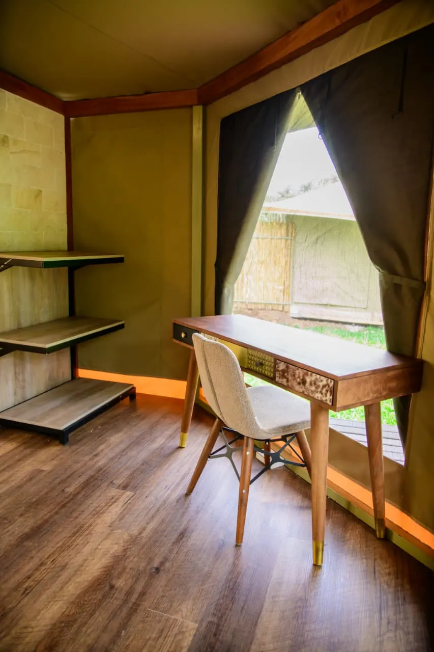 A writing desk and chair at the canvas window of a Lenana tented suite, with open shelving alongside